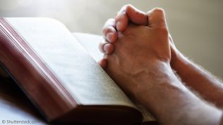 Gefaltete Hände auf einem Gebetbuch
